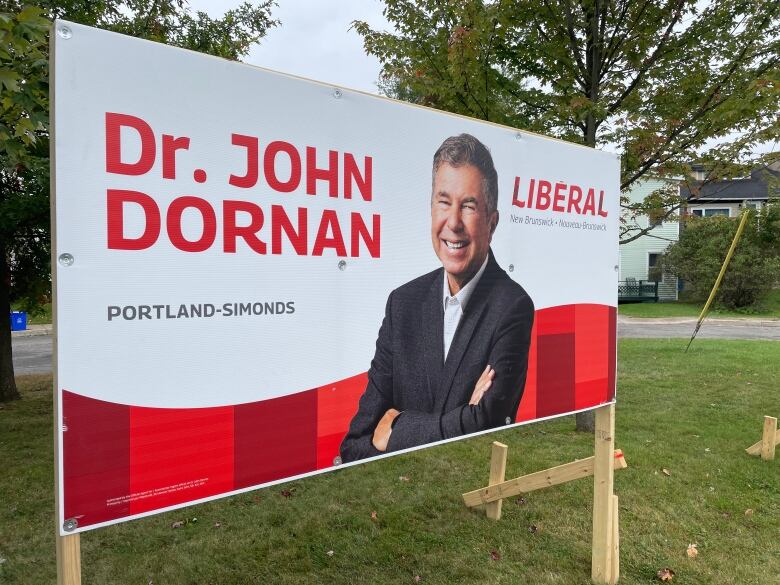 A large billboard stands on a grassy lawn with the picture of a smiling man on it.