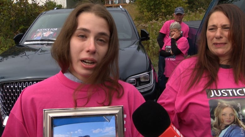 Woman holds picture of two girls crying