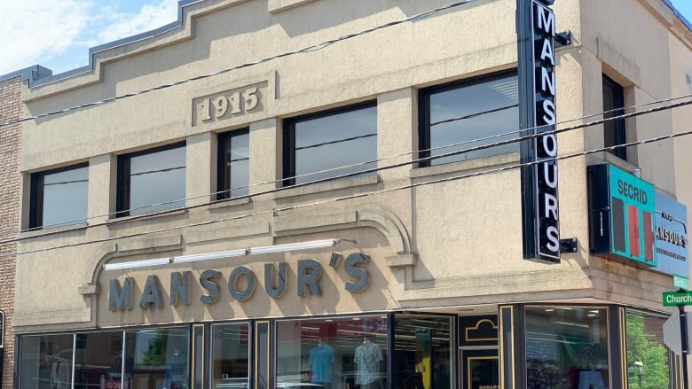 A downtown storefront. Two signs, one horizontal, the other vertical, read MANSOUR'S. The words 1915 can be seen near the top of the building. 