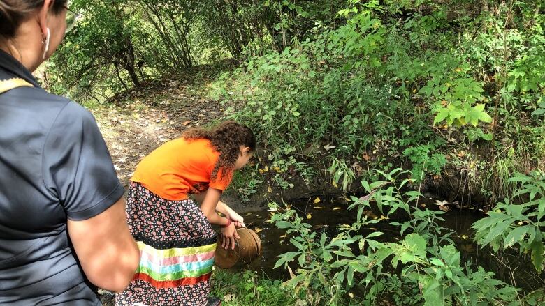 A community member pours water into the Deshkan Ziibi, or Thames River as part of an Indigenous water ceremony. 