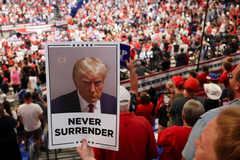 Sign with Trump's mug shot that says 'Never surrender' in front of packed arena