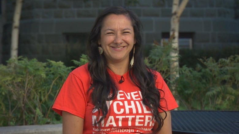 A woman in an orange shirt smiles.