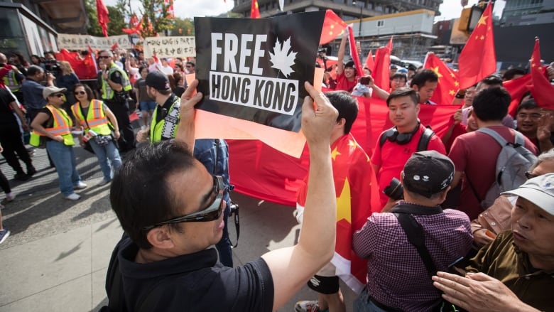 A Hong Kong anti-extradition bill protester holds up a sign in front of pro-China counter-protesters during opposing rallies in Vancouver on Saturday August 17, 2019.