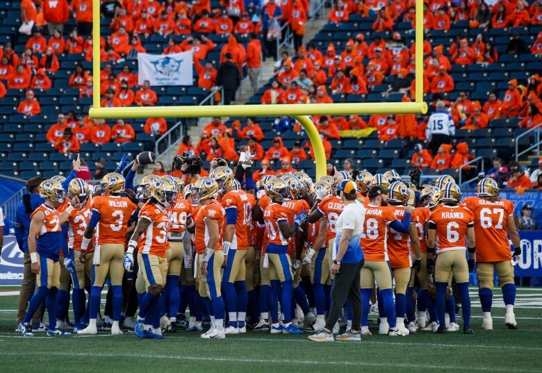 A football team wearing orange jerseys gathers under the goalposts before the game.