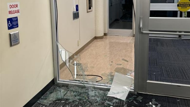 A broken glass door is seen from inside an institutional building.