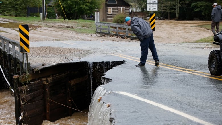 A person leans over the survey a collapsed portion of a bridge.