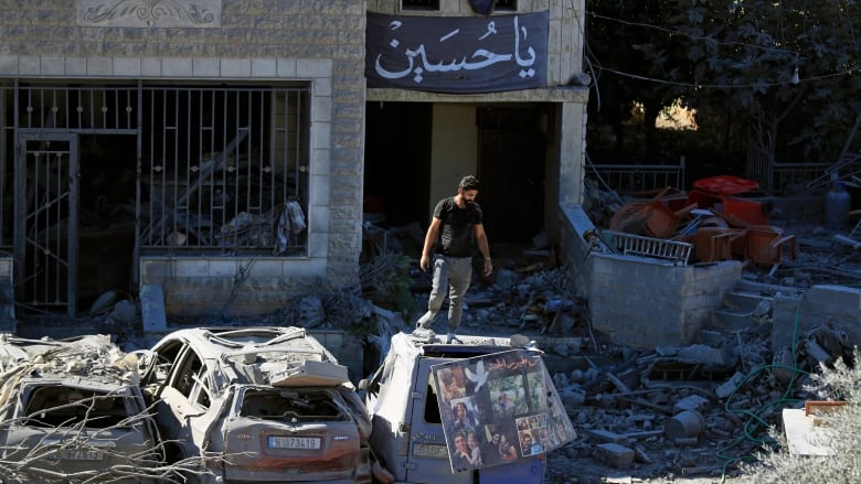  A man stands on top of a damaged car at the site of an Israeli airstrike in Saksakieh, south Lebanon