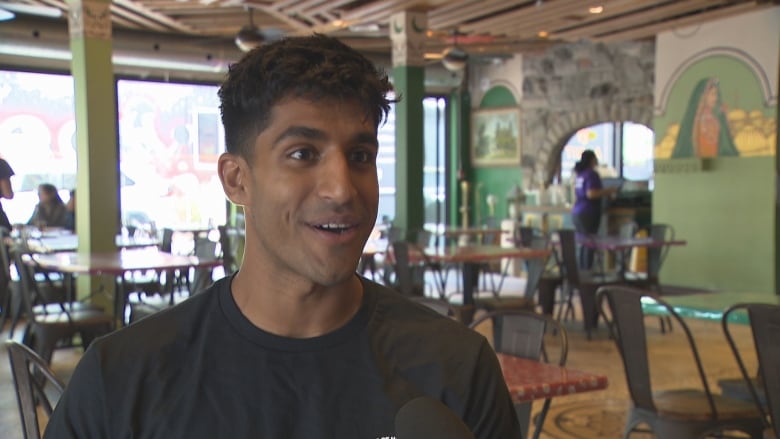 A young man smiles while speaking to a reporter in a restaurant