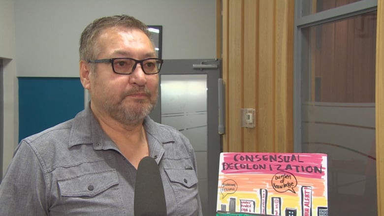 A man standing in front of an illustration which has the words 'consensual decolonization'