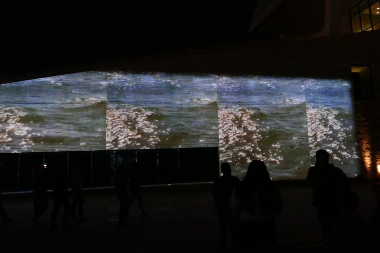 A film showing waves projects onto a building at night. 