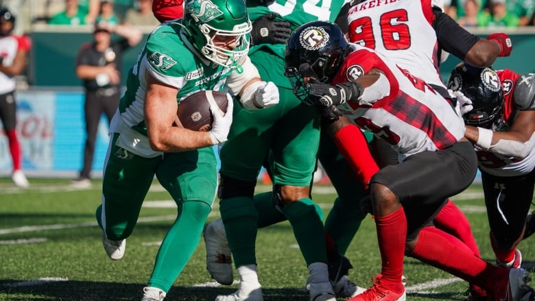 Roughriders player runs with football while Redblacks player tries to stop him.