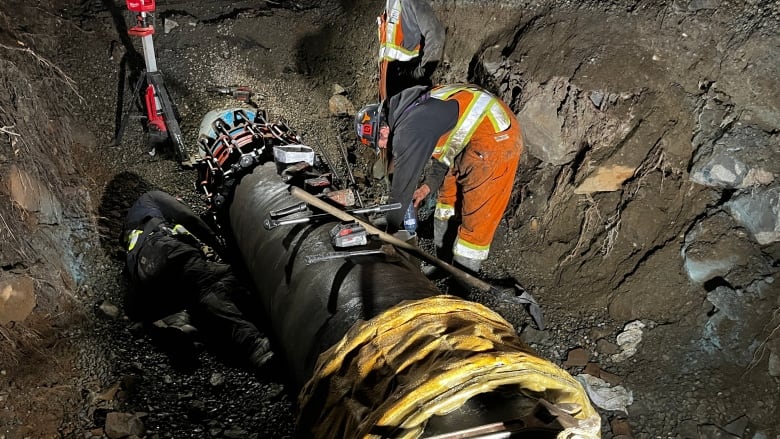 People wearing high-vis vests work on a large pipe in the ground.