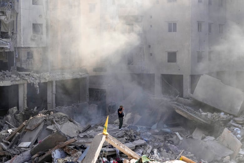 A person stands amid the rubble of a destroyed building.