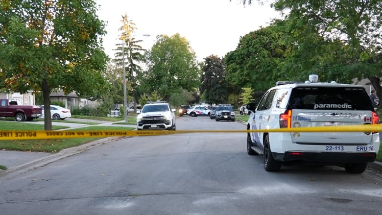 Police tape runs across a residential street where multiple police vehicles are parked in the late evening