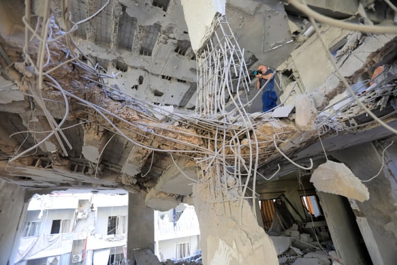 A man, holding a camera, stands amid the rubble of a destroyed building and takes a photo.