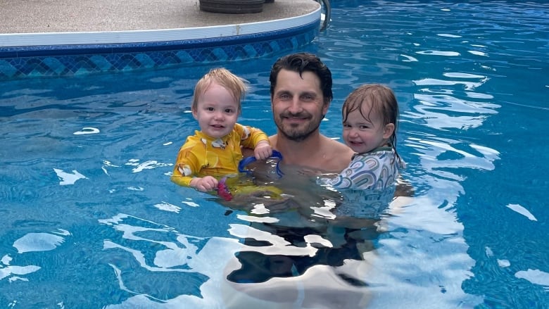 A man in an outdoor pool holds two children.