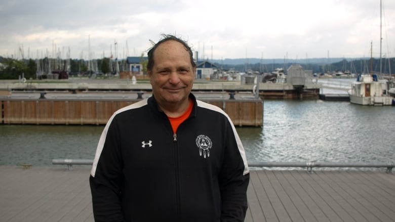 A person in a black under armour jacket smiles in front of several boats, docks and the water.