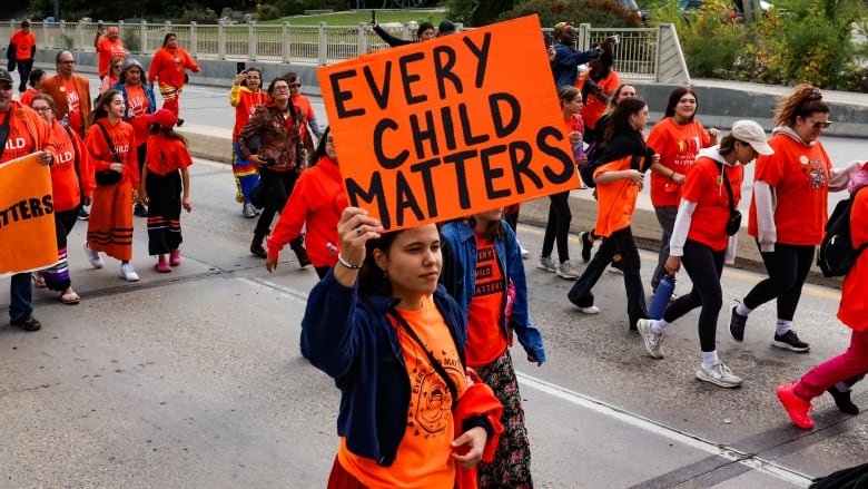 A woman holds up a sign that says 'Every Child Matters'