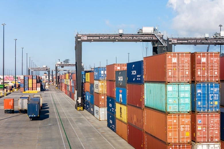 A long row of shipping containers are seen on a dock.