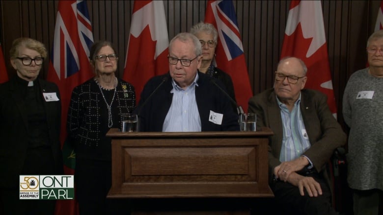 A man stands behind a podium with several others standing behind him. 