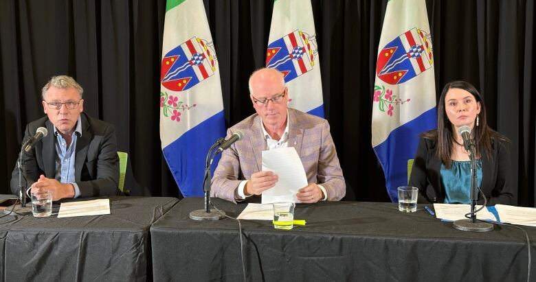 Two men and a woman sit behind a table at microphones.