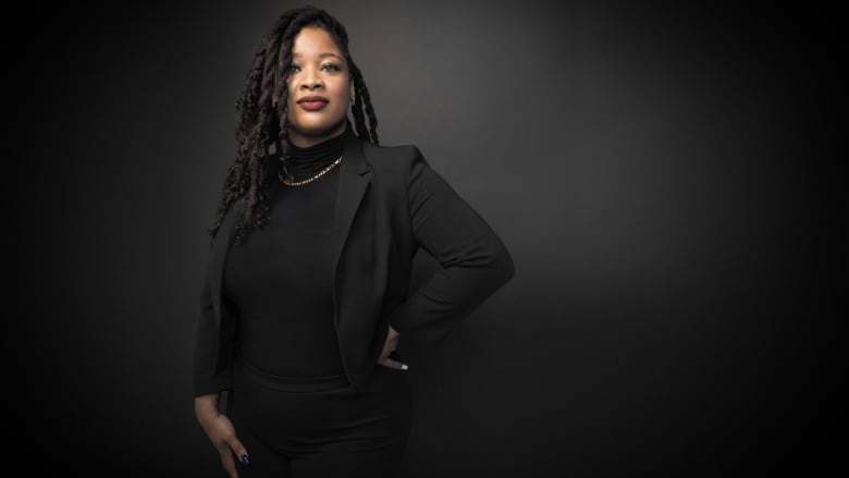 A woman stands in front of a black background.