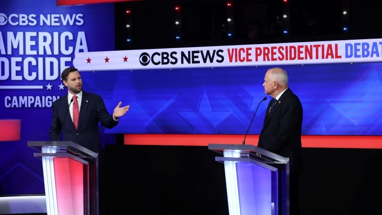 Two men in suits stand behind podiums. The sign behind them says, 