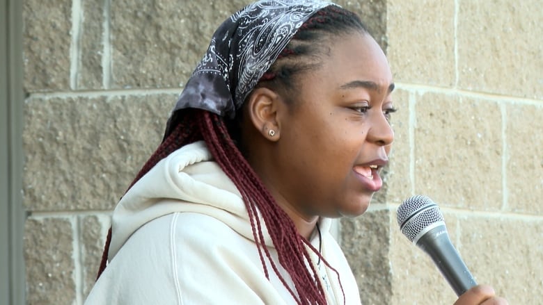 A woman wearing a white hoodie speaks into a microphone.