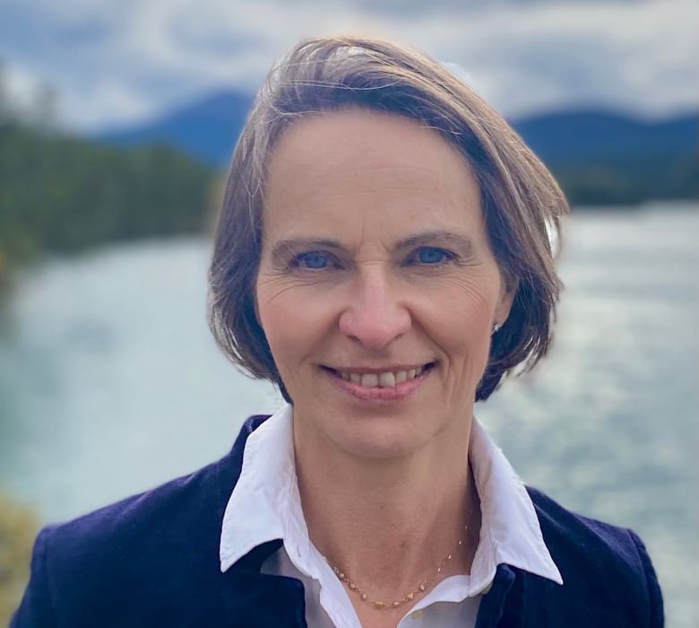 A woman smiles in front of a scenic background.