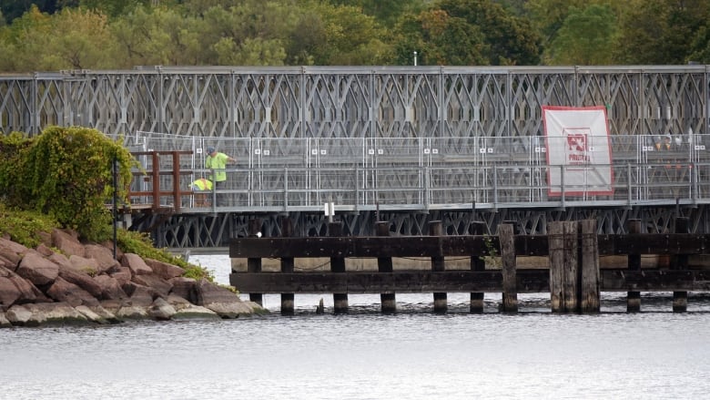 Two people in reflective shirts stand on a temporary bridge over a body of water, near the shore.