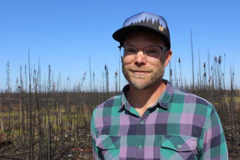 A man wearing glasses, ball cap and plaid shirt.