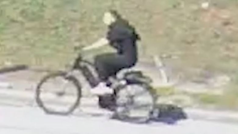 Screengrab of video of a suspect in a North Vancouver sex assault. Suspect is wearing black clothing and is riding an e-bike.