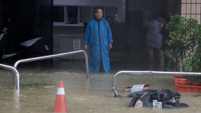 A man in a raincoat looks at flooded roads