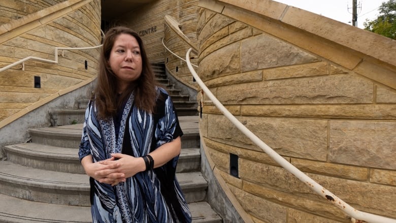 A woman stands on the steps of a building outdoors.