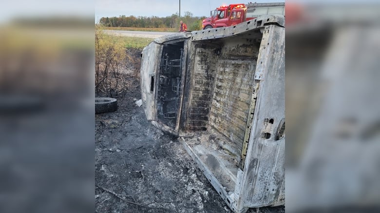 A charred pickup truck lies on its side in a ditch