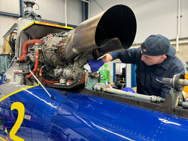 A man is shown in a baseball cap and rubber gloves wiping a cloth on a shiny helicopter.