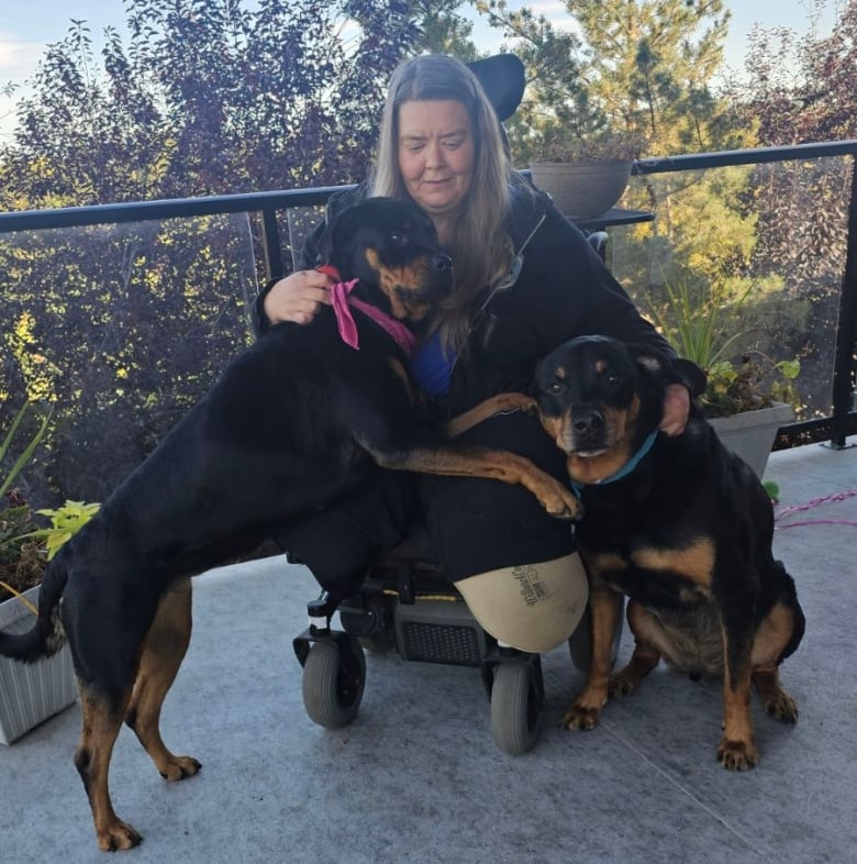 Marla Smith sits in her power wheelchair on her balcony with her service dogs Kuno and Chesnyy by her side. 