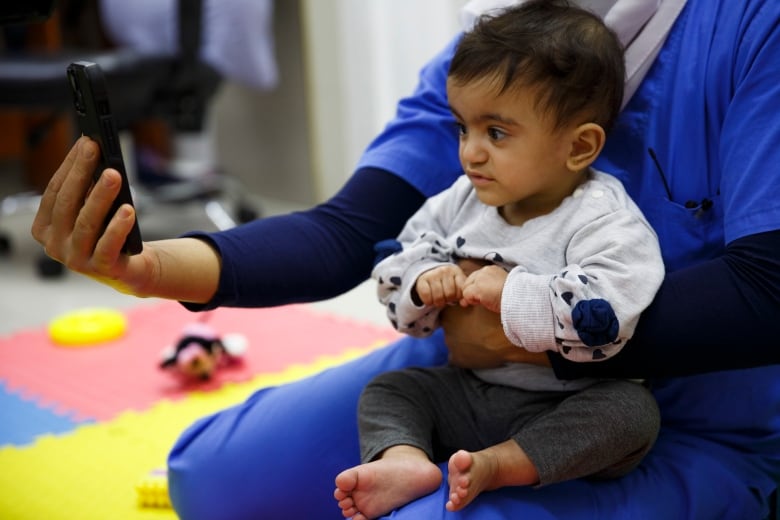 A nurse holds up a phone for in front of a baby