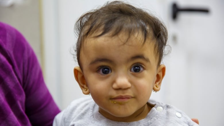 A baby in a grey shirt looks at the camera