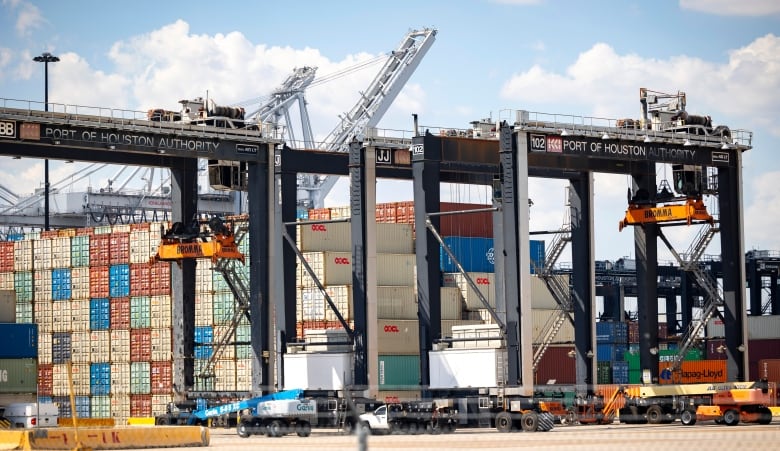 A tall metal structure towers over an enormous stack of colourful shipping containers. Trucks and other vehicles are visible at the bottom, looking very small. 