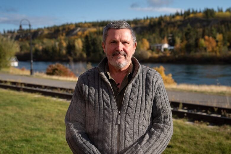 A man in a sweater stands by a river.