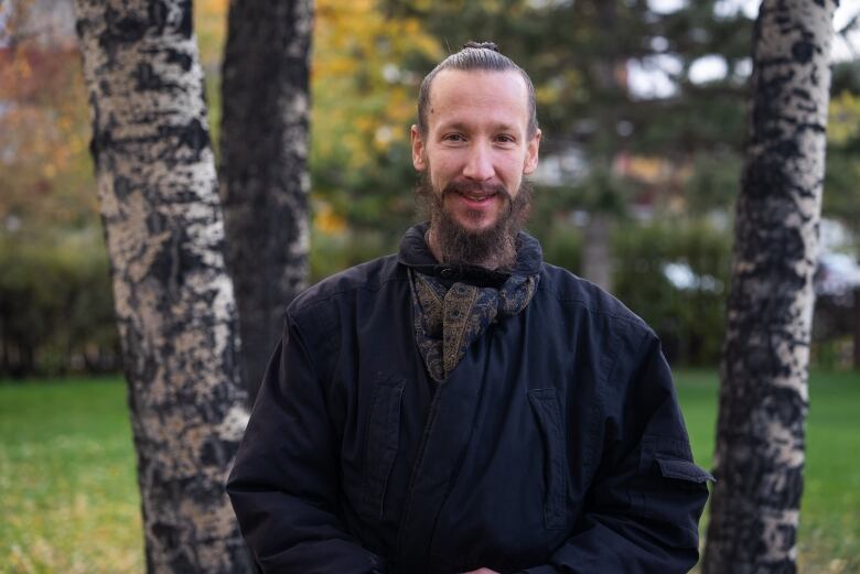 A man stands in front of some grass and trees.