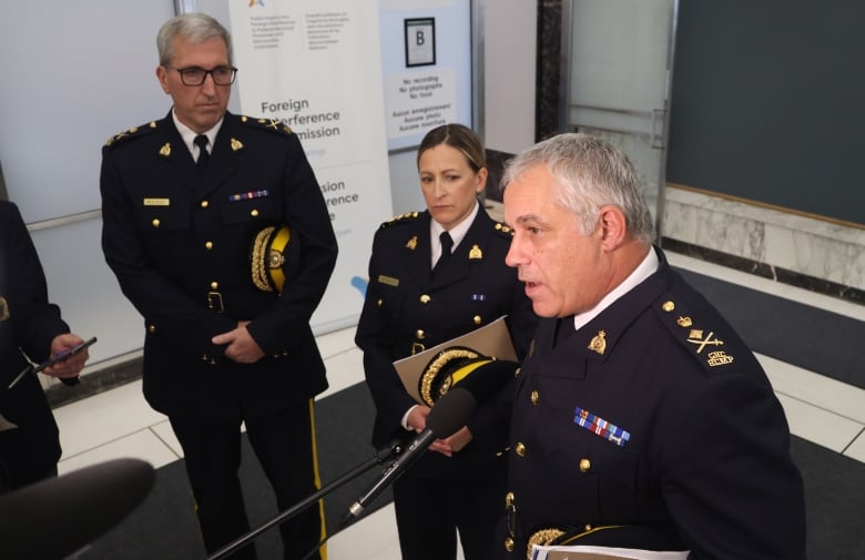 Three uniformed RCMP officers speak with reporters.