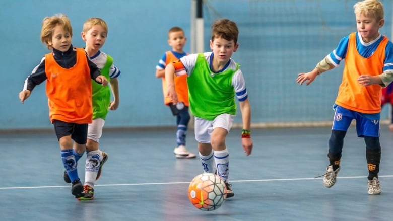 Young children chase a soccer ball in a gymnasium