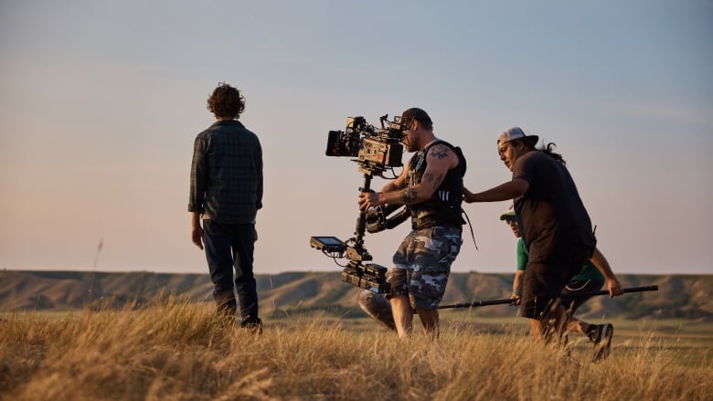 Two camera guys film a man standing atop a prairie valley.