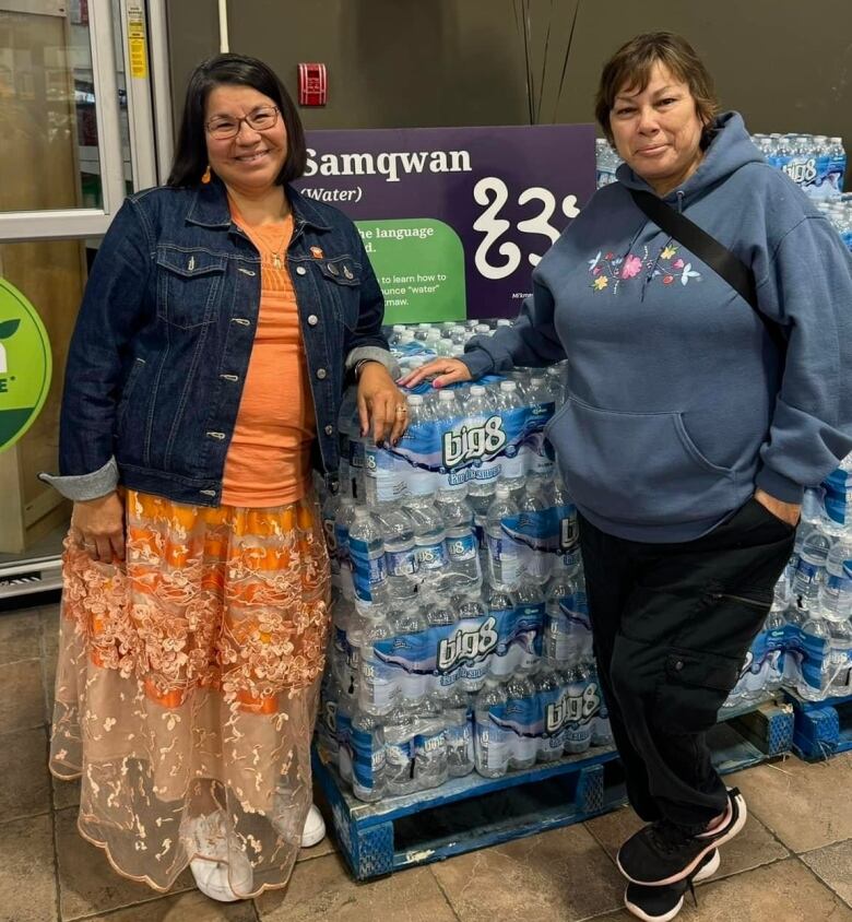 two women standing next to bottles of water at grocery store