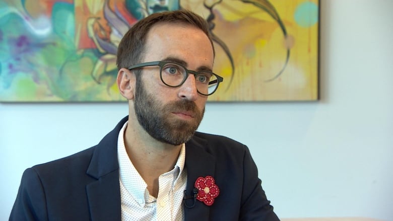 A man in a collared shirt and suit jacket with a red flower on the lapel