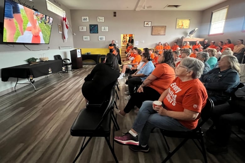 People wearing orange sit in a room to watch a video.