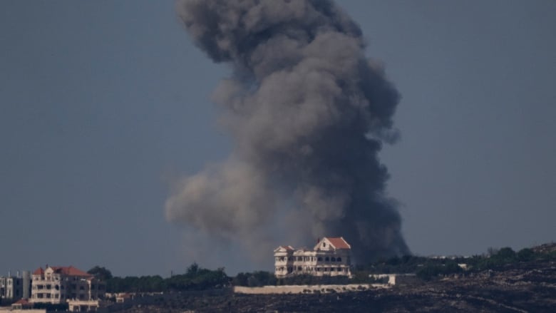 Billows of dark smoke rise on a landscape behind a building.