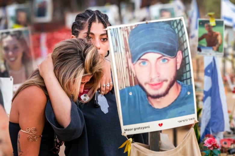 People embrace and grieve behind a poster sign featuring a person's portrait.